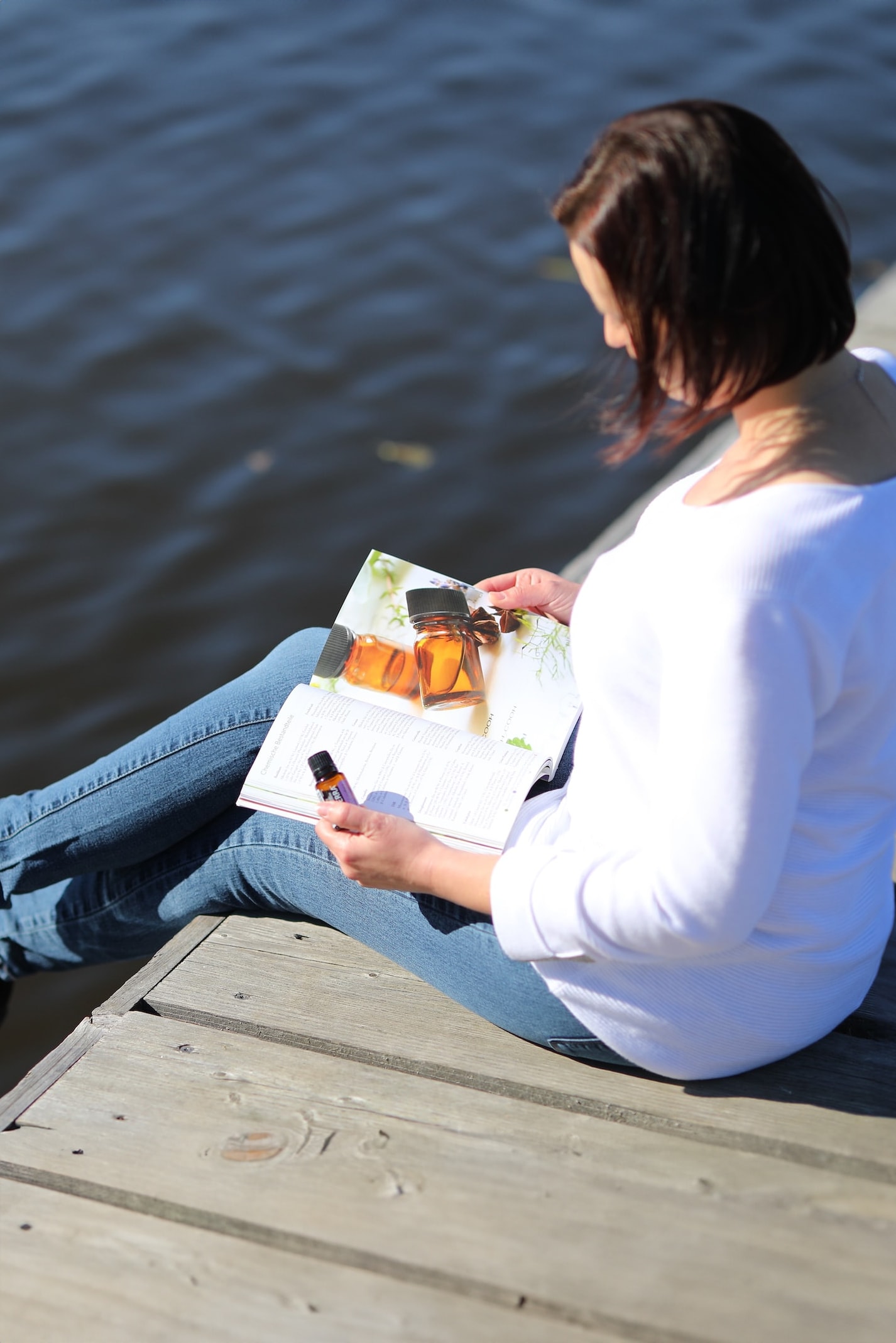 Jessy Richter sitzend am Wasser mit Buch und Ölflasche in der Hand