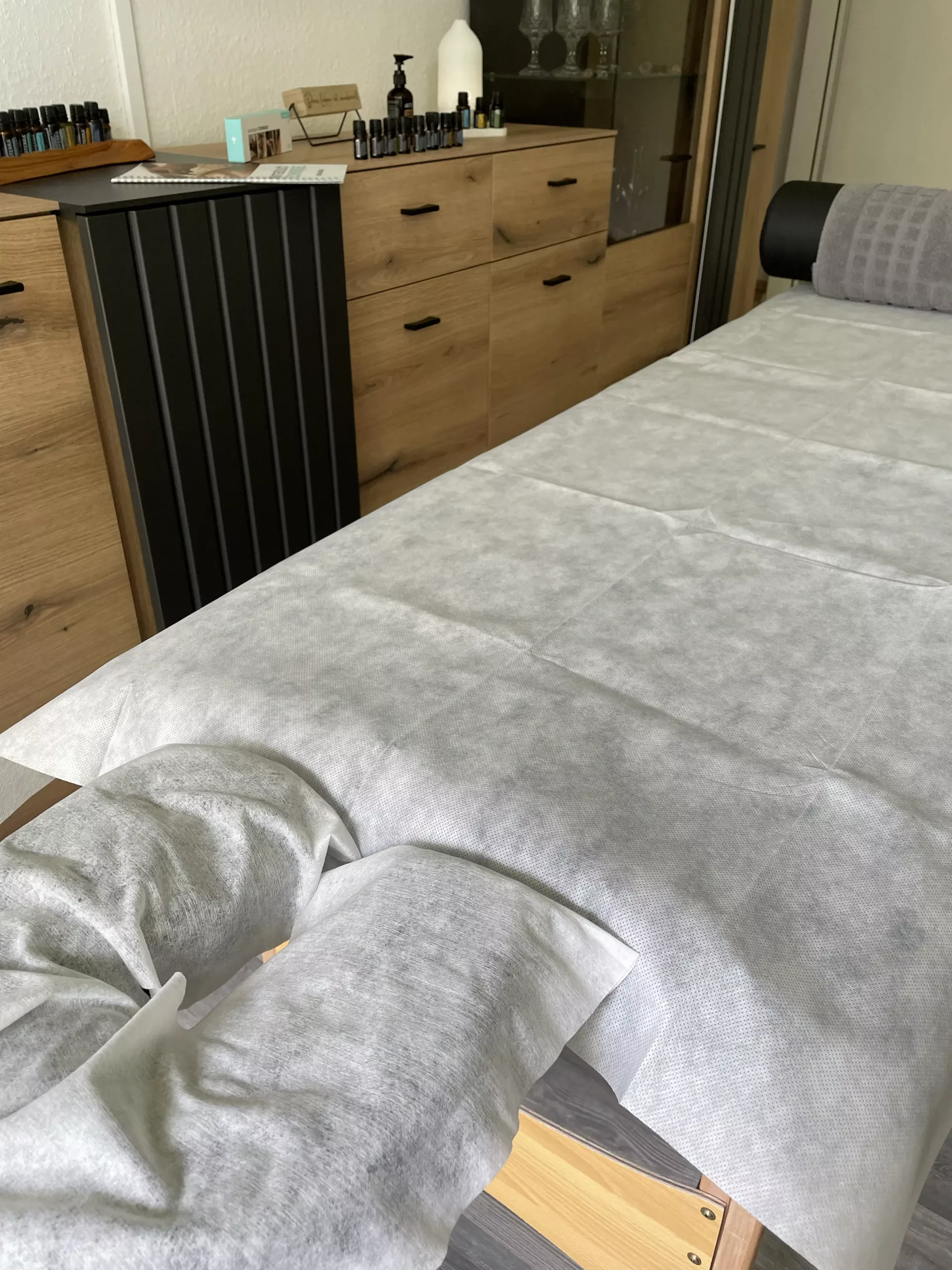 AromaTouch Behandlungsliege mit den verschiedenen AromaTouch Ölen im Hintergrund für die Anwendung